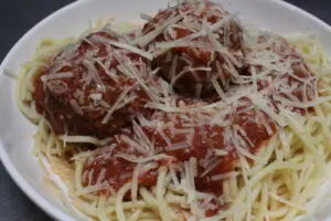 A plate of spaghetti and meatballs with parmesan cheese.
